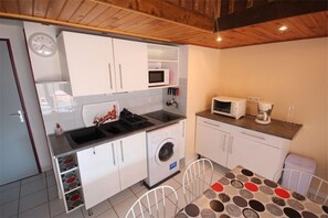 A compact kitchen with white cabinets, a microwave, a washing machine, and a small dining table with a patterned tablecloth.