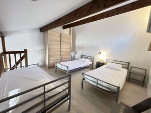 A room with two beds, a wooden ceiling beam, a radiator, and a bedside table with a lamp.