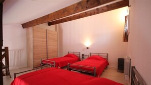 A room with two beds, wooden beams, a radiator, and a wall-mounted light fixture.