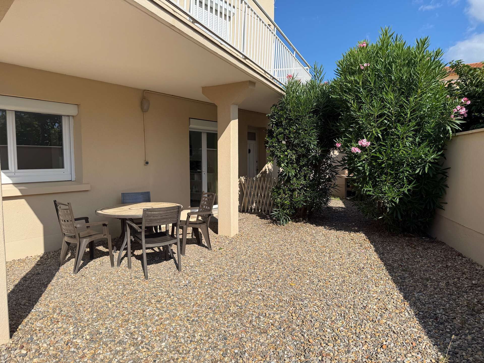 A patio with a table and chairs, a white fence, and a small tree with pink flowers.