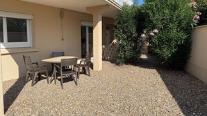 En terrasse med et bord og stole, et hvidt hegn og et lille træ med lyserøde blomster.