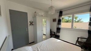 Et soveværelse med seng, garderobeskab, stol, et vindue med gardiner og en hængende lampe.