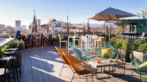 A rooftop terrace with outdoor seating, including wicker chairs and tables, and a view of the city skyline. - Occidental Diagonal 414 (Barcelona)