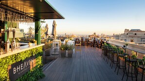 A rooftop bar with a view of the city skyline, featuring a bar counter, seating area, and potted plants. - Occidental Diagonal 414 (Barcelona)