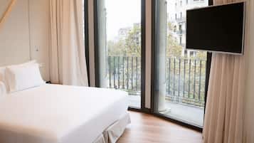 A hotel room with a large bed, a TV mounted on the wall, and a balcony with a view of the city.