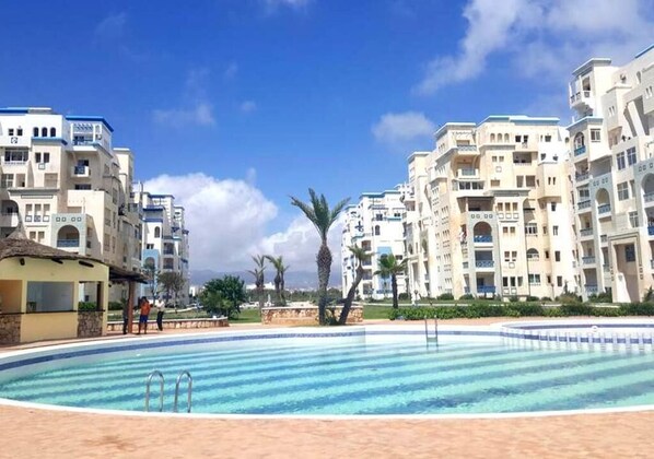 Relax by the large pool surrounded by a sandy beach and multi-story buildings with balconies.