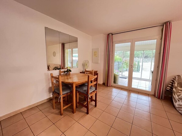 A dining area with a wooden table and chairs, a large mirror, a fan, and a sliding glass door leading to an outdoor area.