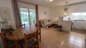 A compact living space with a dining area, a sofa, a small table, a kitchen with a dishwasher, and a sliding glass door leading to an outdoor area. - Nice villa in residence CLOS DE SOCORRO with pool, 2 bedrooms, great View, PORTIRAGNES PLAGE (PORTIRAGNES)