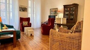 Un salon chaleureux avec un fauteuil rouge, une chaise en osier, un canapé vert et un meuble en bois.
