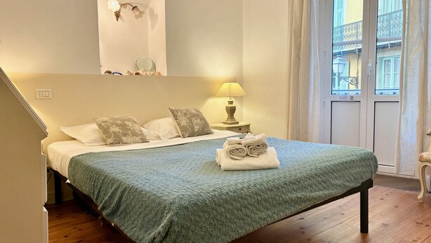 Un lit bien fait, recouvert d’une couverture verte, avec deux oreillers et une serviette enroulée posée sur le lit. Une table de chevet avec une lampe se trouve à côté du lit.