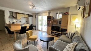 Un salon moderne avec un canapé gris, une petite table ronde et un coin repas comprenant une table et des chaises en bois.