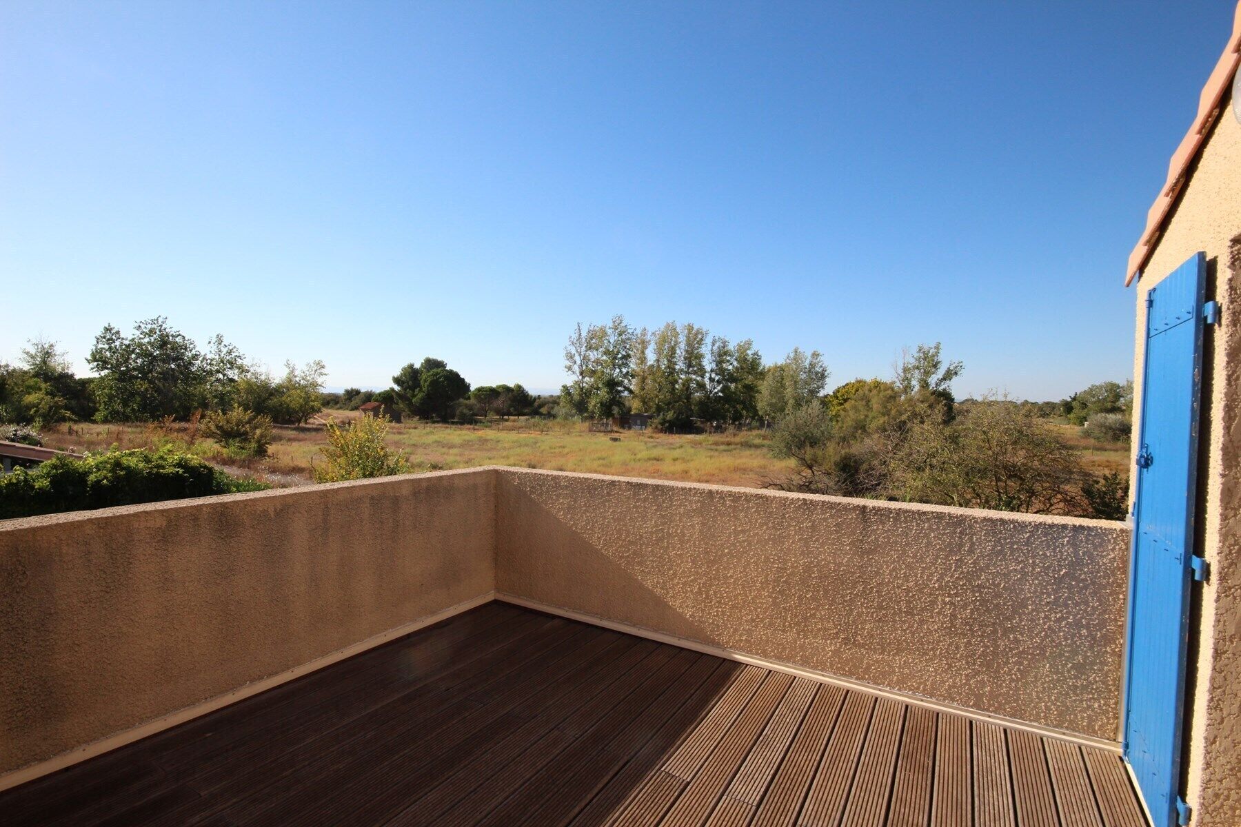 Un balcon donnant sur un paysage rural, une porte bleue et un plancher en bois.
