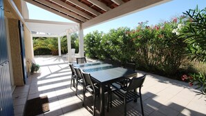 Une terrasse extérieure dotée d’un espace salon abrité, d’une table et de chaises.