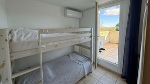 Une chambre avec un lit superposé, une fenêtre, un ventilateur de plafond et une porte donnant sur un balcon extérieur.