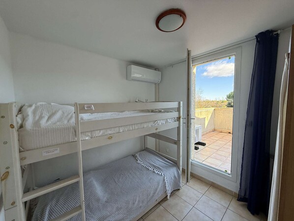 A bunk bed room with a window, a ceiling fan, and a door leading to an outdoor balcony. - Spacious corner villa with nice view on natural reserve, 3 bedrooms, AIRCO, PORTIRAGNES PLAGE (PORTIRAGNES)