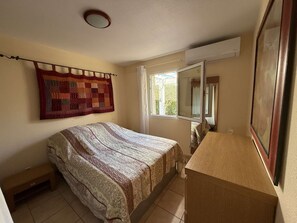 Une chambre à coucher avec un lit, une fenêtre, un miroir et une courtepointe accrochée au mur.