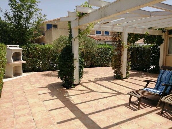 A covered patio area with a barbecue grill, a pergola, and a seating area with a chair and a table. - Spacious corner villa with nice view on natural reserve, 3 bedrooms, AIRCO, PORTIRAGNES PLAGE (PORTIRAGNES)