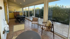 Une terrasse ensoleillée avec une table à manger, des chaises et une vue sur le jardin.