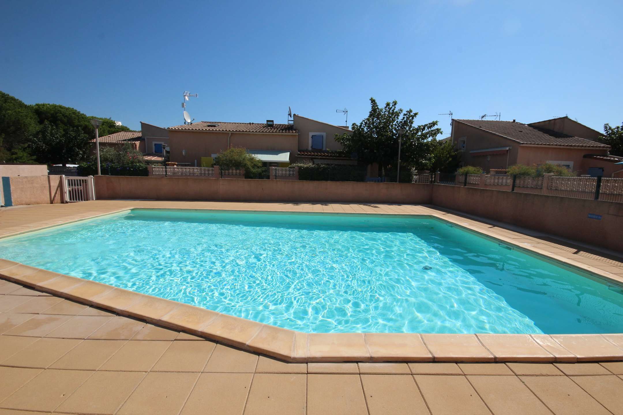 A rectangular swimming pool with clear blue water, surrounded by a tiled deck and a low brick wall.