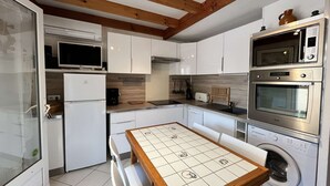 Eine kompakte Küche mit weißen Schränken, einer Mikrowelle, einem Backofen, einem Geschirrspüler und einem gefliesten Tisch.