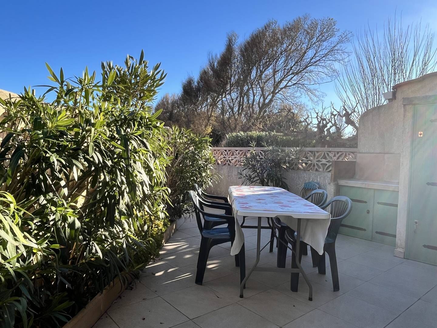 Un patio al aire libre con una mesa y sillas, rodeado de follaje y un muro decorativo.