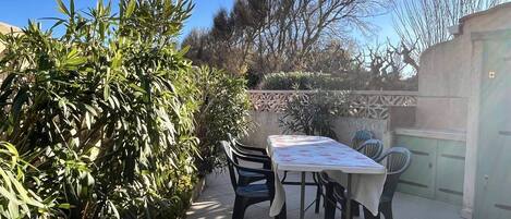 Un patio al aire libre con una mesa y sillas, rodeado de follaje y un muro decorativo.