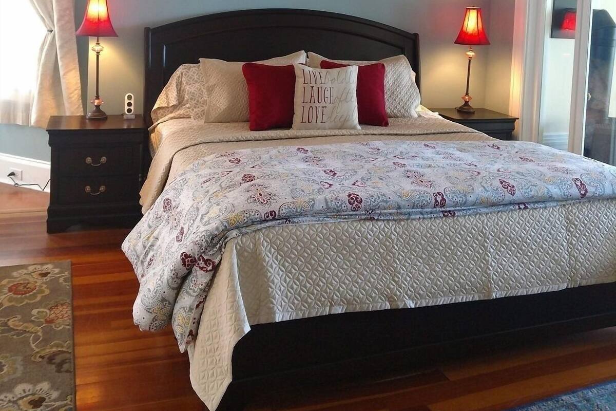 A bedroom with a bed, two bedside tables with lamps, a painting on the wall, and a view through a door.
