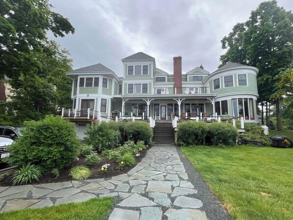 A large, multi-story house with a prominent front porch, a stone pathway leading to the entrance, and a well-maintained garden.