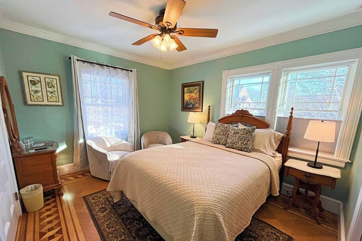 A bedroom with a bed, a ceiling fan, a chair, a nightstand, and a window.