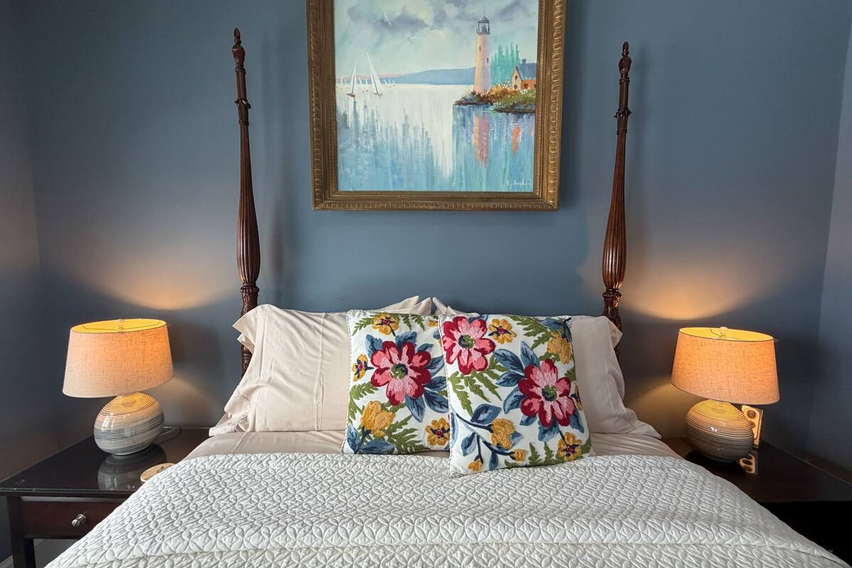 A bedroom with a bed, two nightstands, a painting, and a lamp.