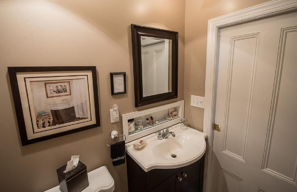 A bathroom with a sink, mirror, framed artwork, and a door.