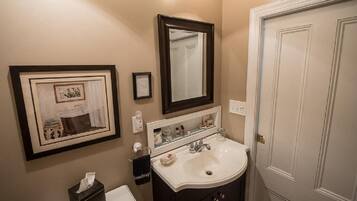 A bathroom with a sink, mirror, framed artwork, and a door.
