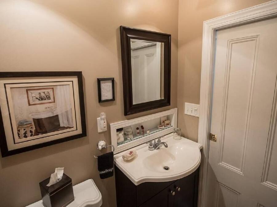 A bathroom with a sink, mirror, framed artwork, and a door.
