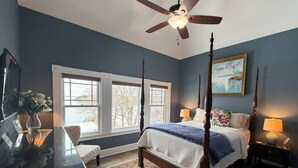 Un dormitorio con una cama con dosel, un ventilador de techo, un ventanal grande y un cuadro en la pared.