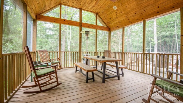 Una terraza de madera con una mesa y sillas, rodeada de amplios ventanales que dan a un bosque.