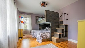 Un dormitorio con literas, una escalera de madera, un escritorio y una ventana con cortinas.