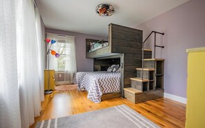 Une chambre avec un lit superposé, un escalier en bois, un bureau et une fenêtre avec des rideaux.