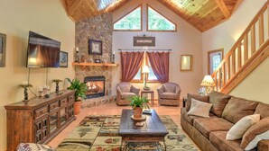 A cozy living room with a stone fireplace, wooden ceiling, and a large window. - Harrah's/Cherokee/Lakes/rafting/ fishing/hiking/waterfall/Elk/rejuvenating peace (Maggie Valley)