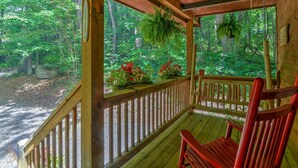 A wooden porch with a red chair, surrounded by lush greenery and a view of a forested area. - Harrah's/Cherokee/Lakes/rafting/ fishing/hiking/waterfall/Elk/rejuvenating peace (Maggie Valley)