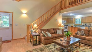 A cozy living room with a wooden staircase, a sofa set, a coffee table, and a kitchen in the background. - Harrah's/Cherokee/Lakes/rafting/ fishing/hiking/waterfall/Elk/rejuvenating peace (Maggie Valley)