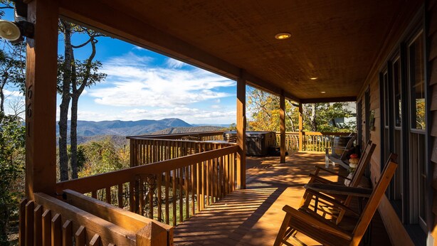 Une terrasse en bois avec une rambarde, un banc et une vue sur les montagnes.