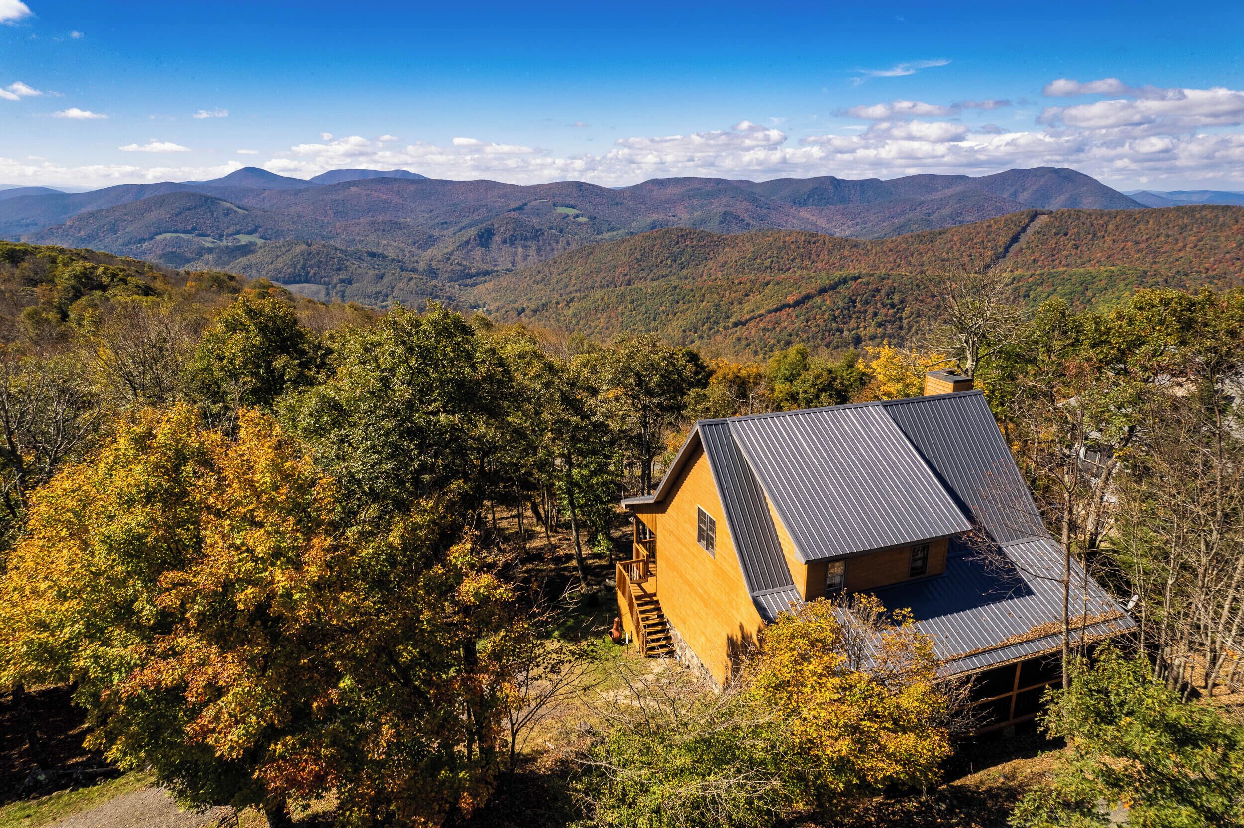 A cabin with a sloped roof, surrounded by forested hills and mountains.