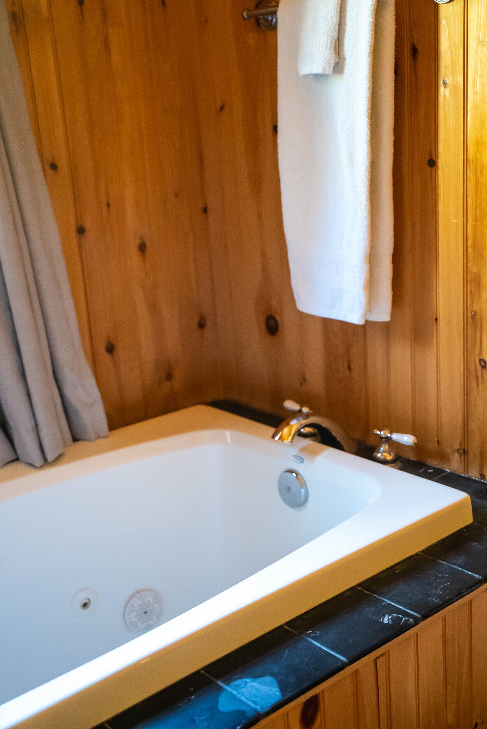 A bathroom with a wooden wall, a white bathtub, and a towel hanging on the wall.