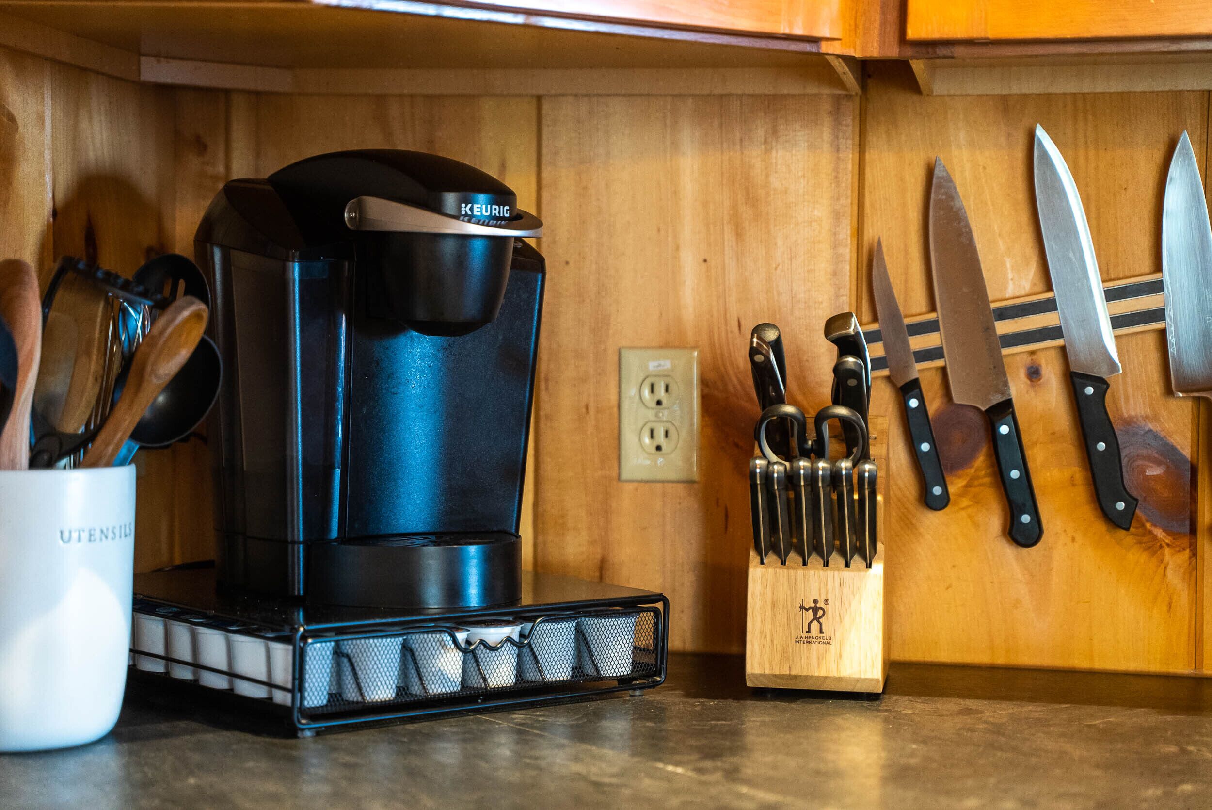 Una cocina con una cafetera Keurig, utensilios y cuchillos sobre la encimera.