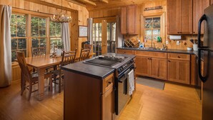 Une cuisine rustique aménagée dans une cabane en bois, avec un îlot central, des placards en bois et une grande fenêtre donnant sur la forêt.