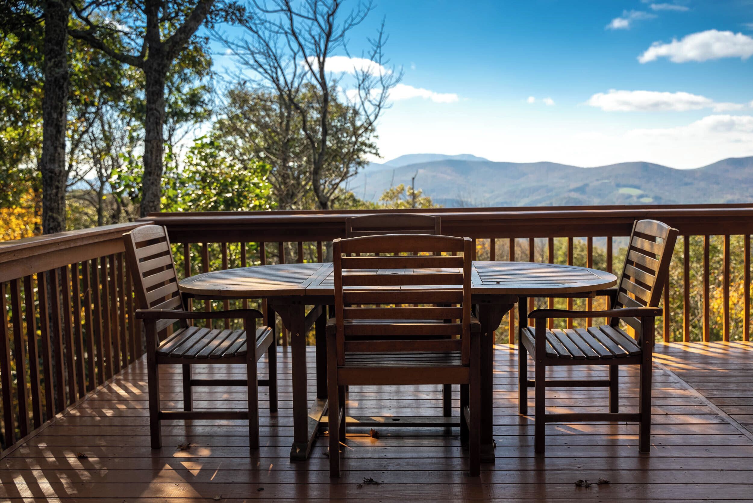Une terrasse en bois avec une table ronde et quatre chaises, offrant une vue sur un paysage montagneux.