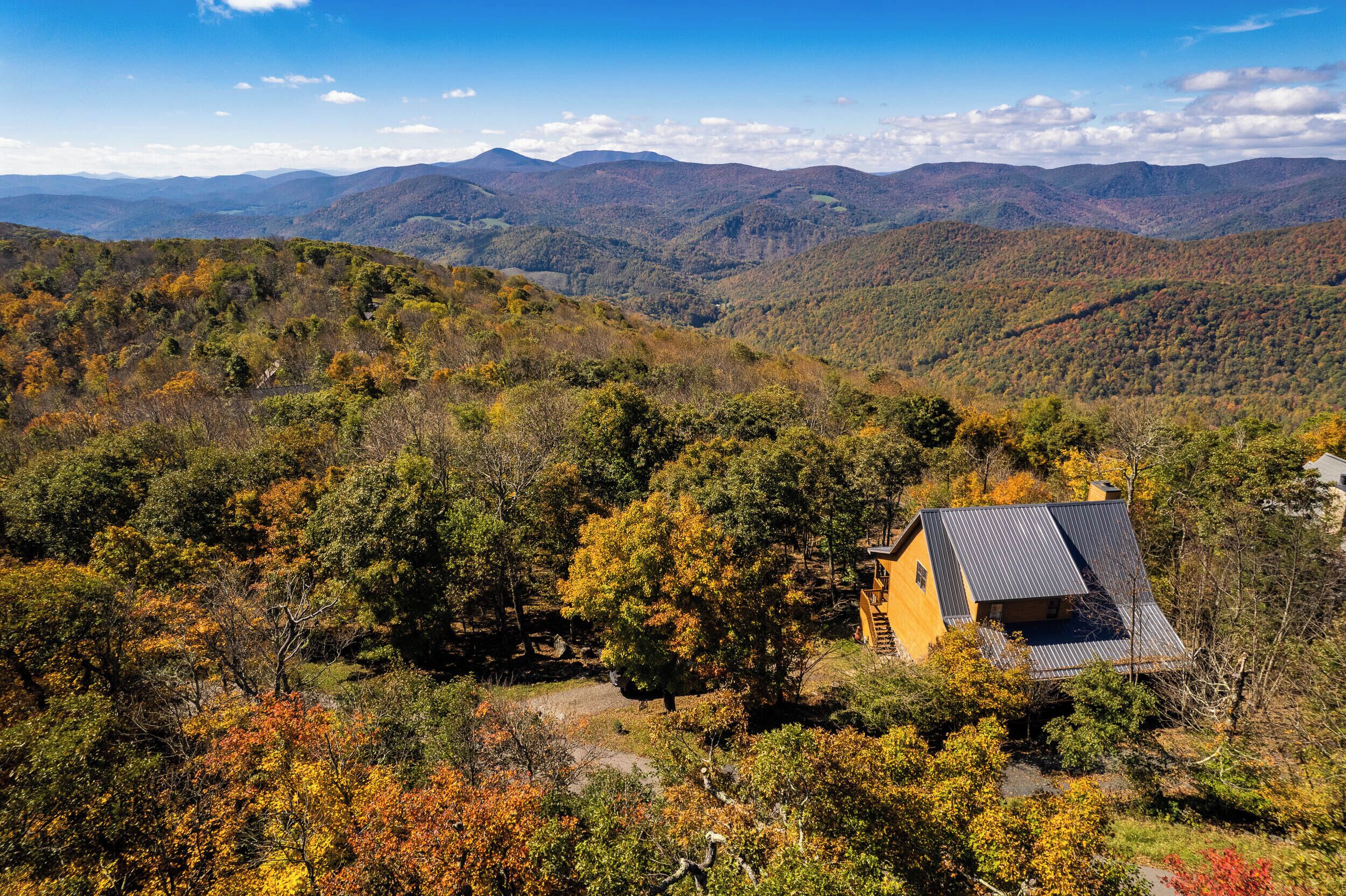 A house with a sloped roof surrounded by autumn-colored trees and mountains in the background.