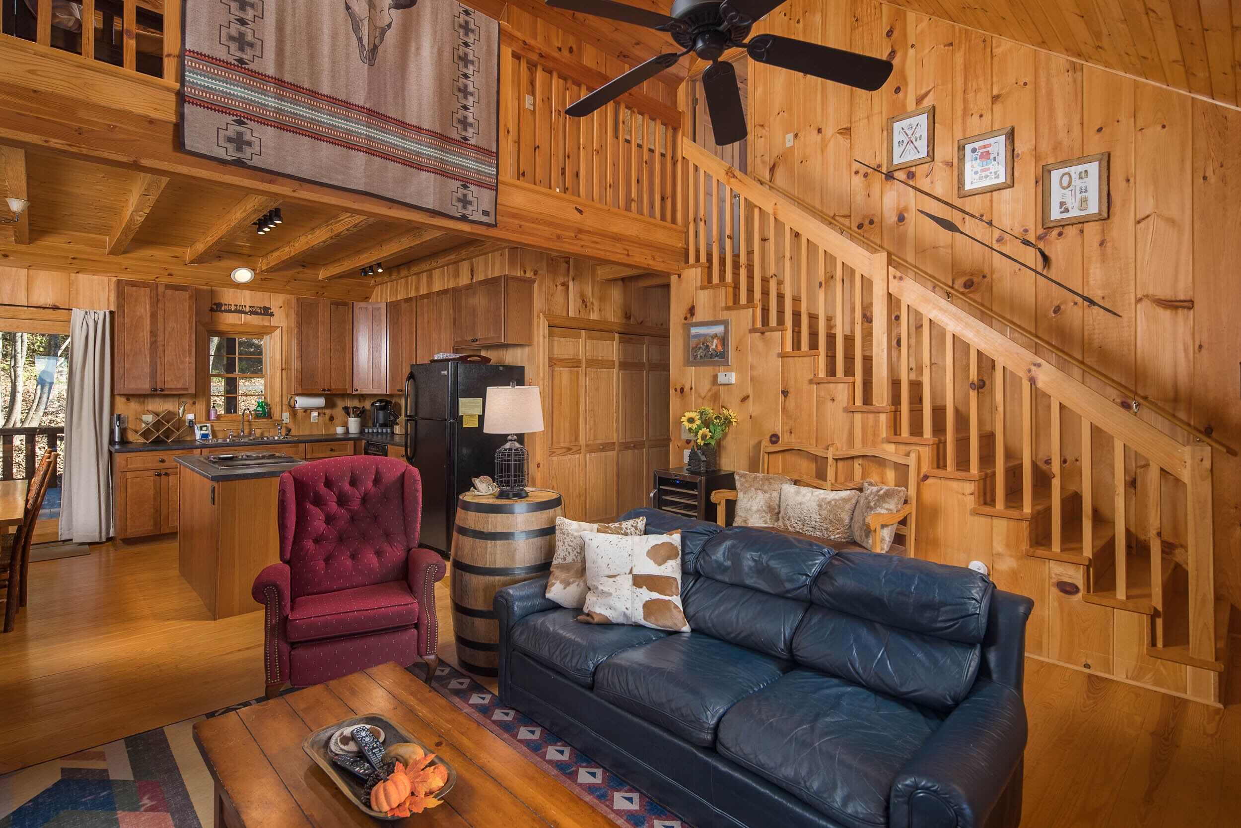 A wooden interior with a leather sofa, a red armchair, and a dining area with wooden cabinets.