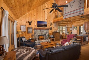Un acogedor interior de cabaña de madera con chimenea, muebles de cuero y ventilador de techo.