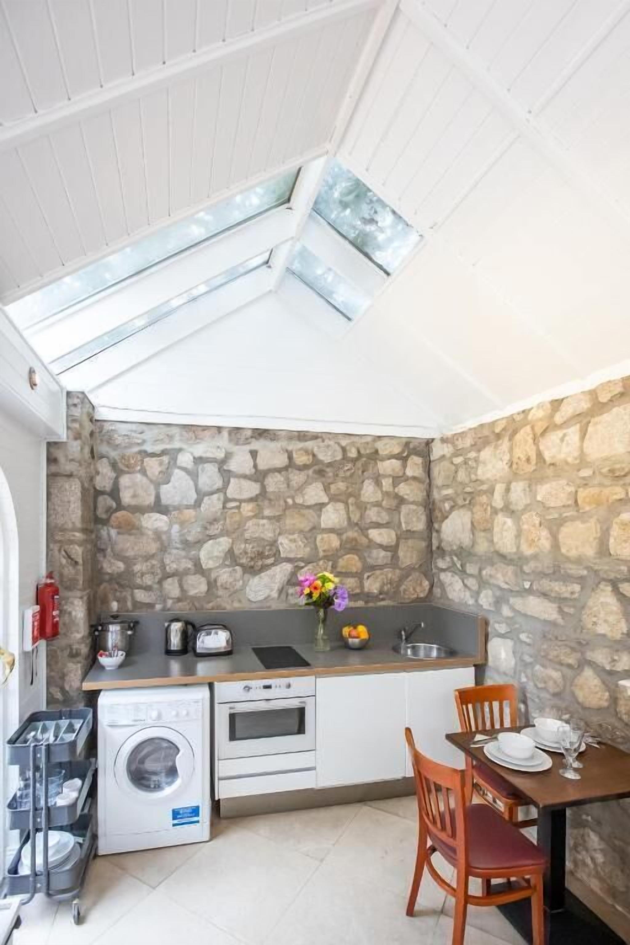 A compact kitchen with a stone wall, a washing machine, a sink, and a dining area with a table and chairs.